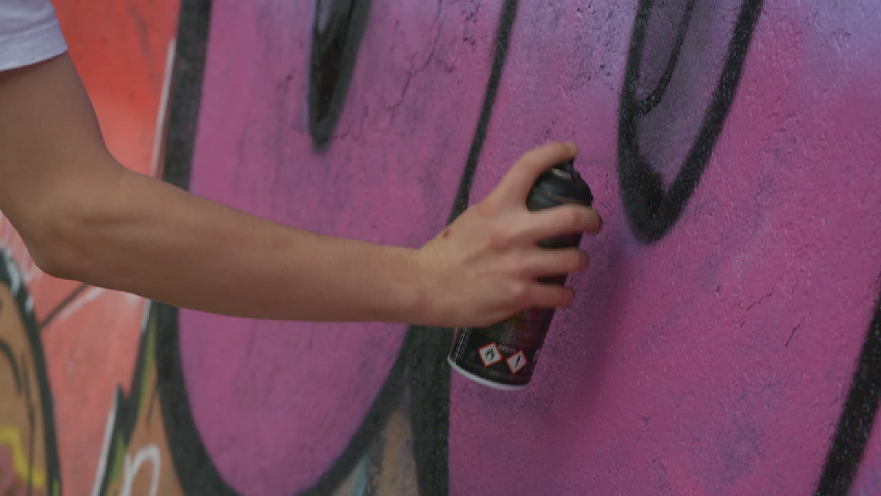 Close up shot of spray paint can graffiti in action. Slow motion as paint is applied to the wall.