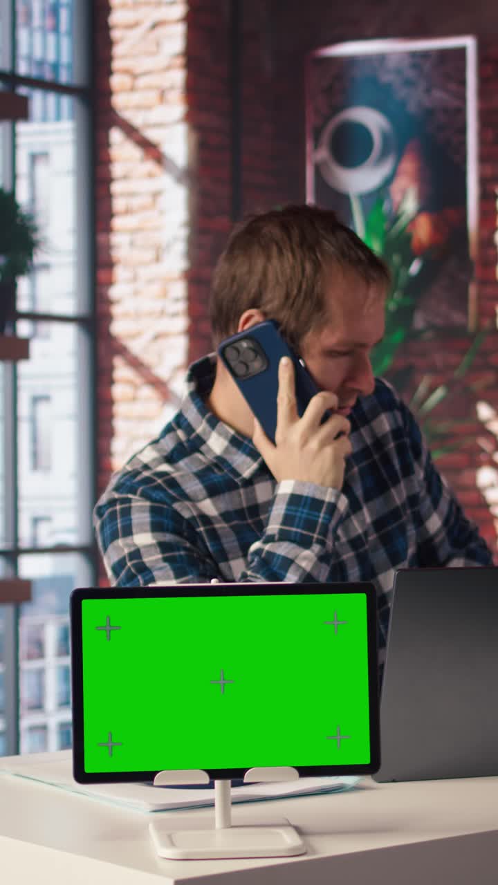 Vertical video Green screen tablet next to man using laptop, answering phone call