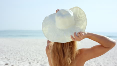 Hermosa-Joven-Poniéndose-Un-Sombrero-Para-El-Sol-En-La-Playa-Vistiendo-Traje-De-Baño-Blanco