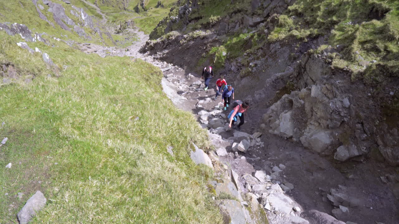 Tilt up shot of group of people climbing, hiking the Carrauntoohil, highest peak in Ireland on a nice sunny day, with epic views in 4K