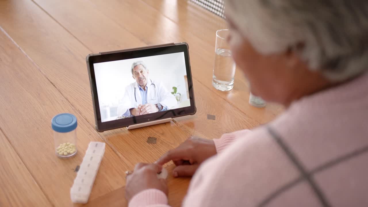 Mulher birracial idosa usando tablet para consulta médica com médico birracial, em câmera lenta.