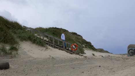 handsome white male walks down sand dune on old wooden stairs to sandy beach