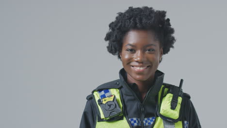 studio portrait of smiling young female police officer against plain background