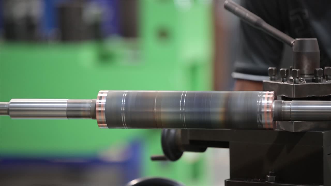 Un cilindro metallico finito tenuto in un mandrino da tornio, che mostra scolorimento da calore e scanalature di precisione.