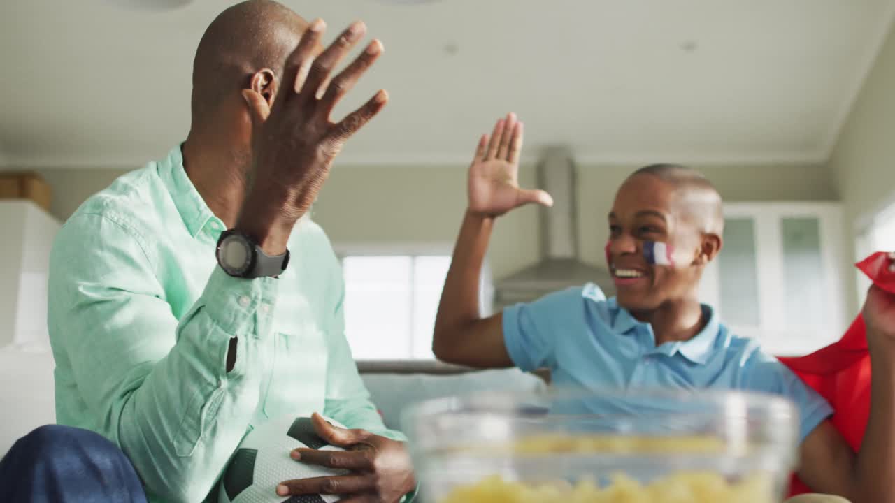 video de padre e hijo afroamericanos con bandera de francia viendo el partido en la televisión