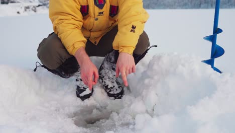 Man-Demonstrating-Size-Of-Fish-In-Ice-Hole-During-Winter