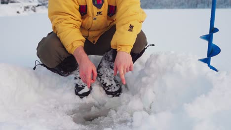 man demonstrating size of fish in ice hole during winter