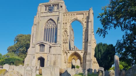 front facade of crowland abbey, england, featuring its bell tower, ancient tombs, and crumbling abbey ruins under a bright blue sky