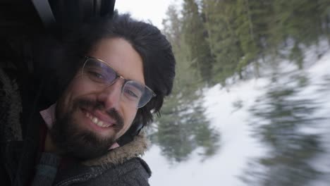 closeup portrait of happy enthusiastic caucasian man with dark hair enjoying sustainable train travel snowy winter landscape, handheld, slow motion, green traveling