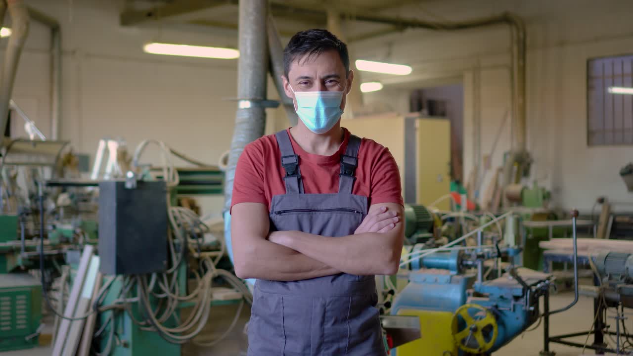 A man in a face mask and overalls stands in a workshop