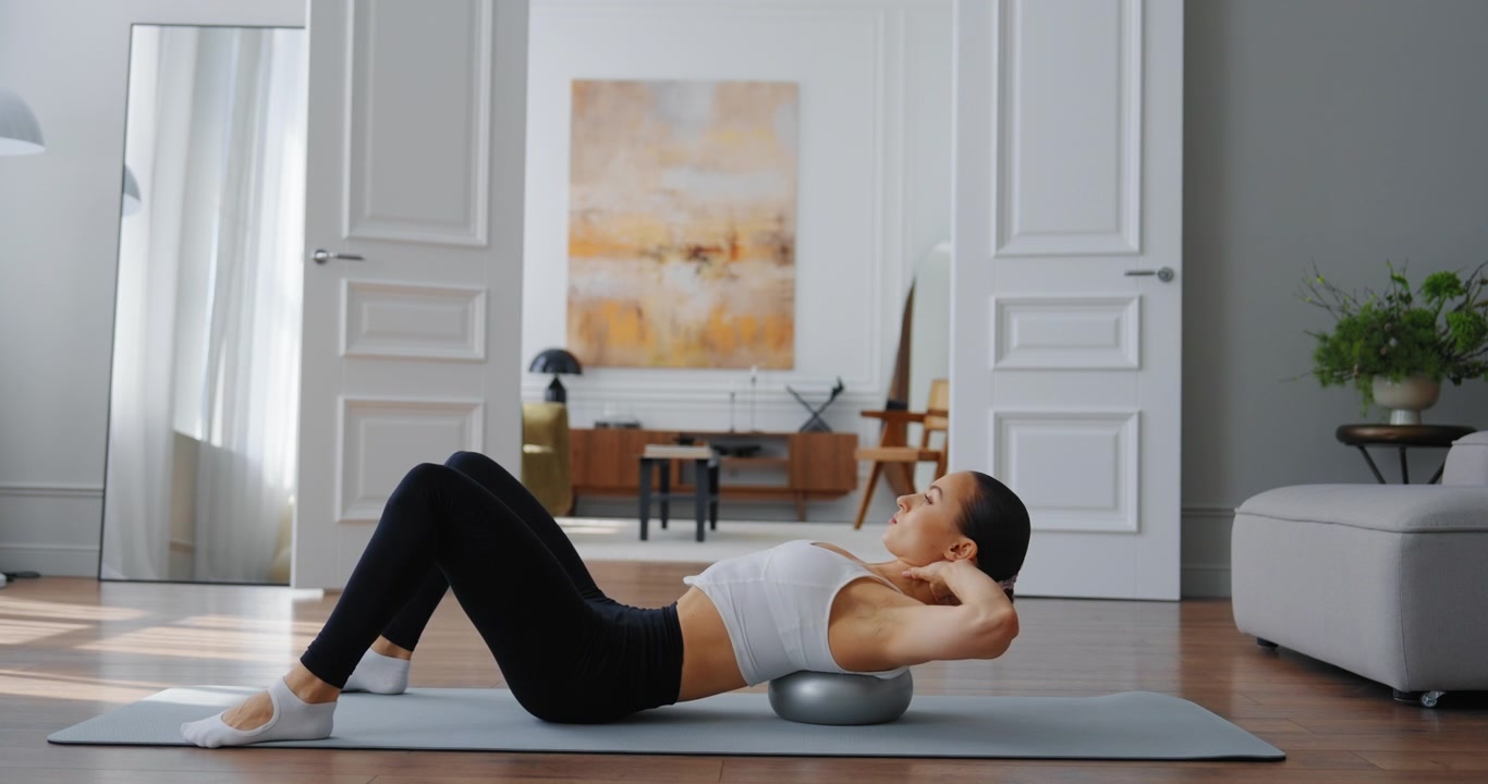 Junge Frau macht Rumpfübungen mit Fitnessball zu Hause