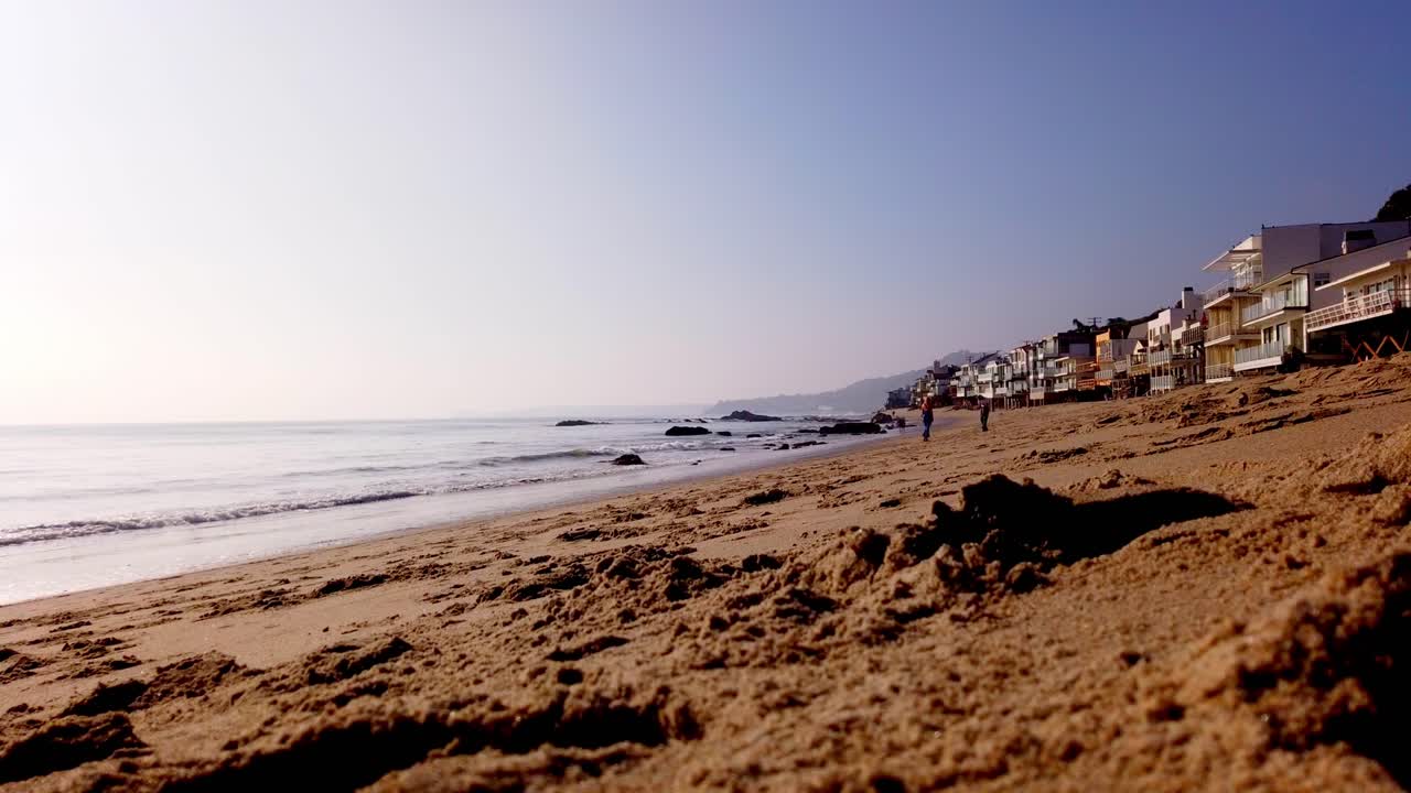 Timelapse de gente caminando por la playa en Malibú en una zona residencial.