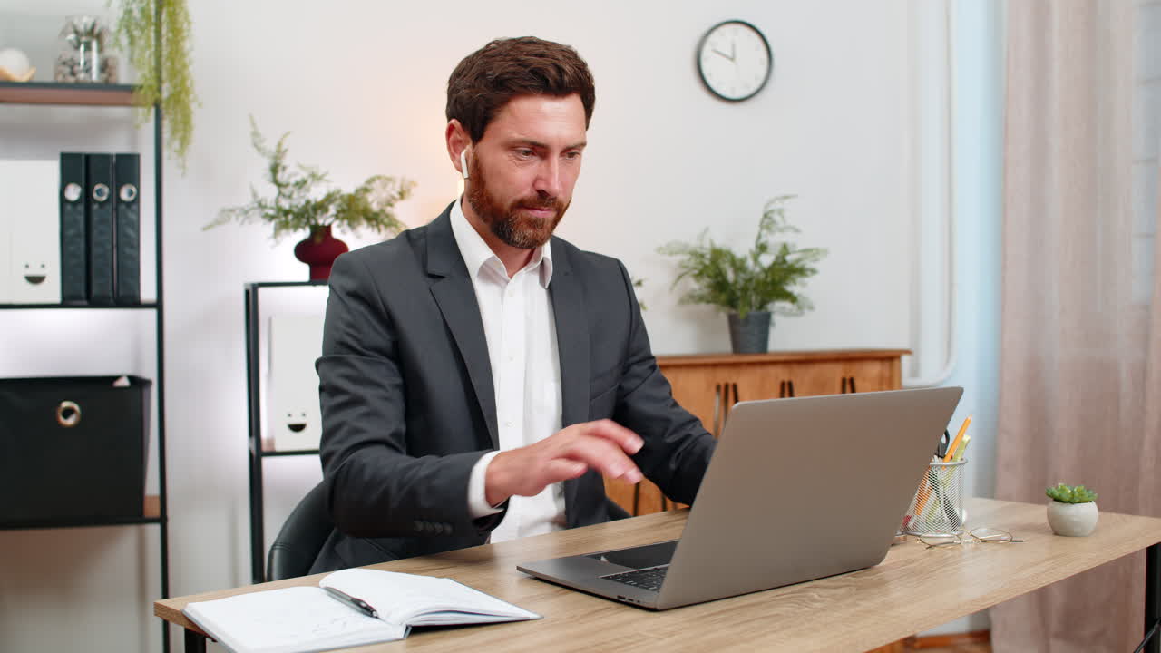 Middleaged businessman attends webinar on laptop wears earphones takes notes snaps smartphone photo