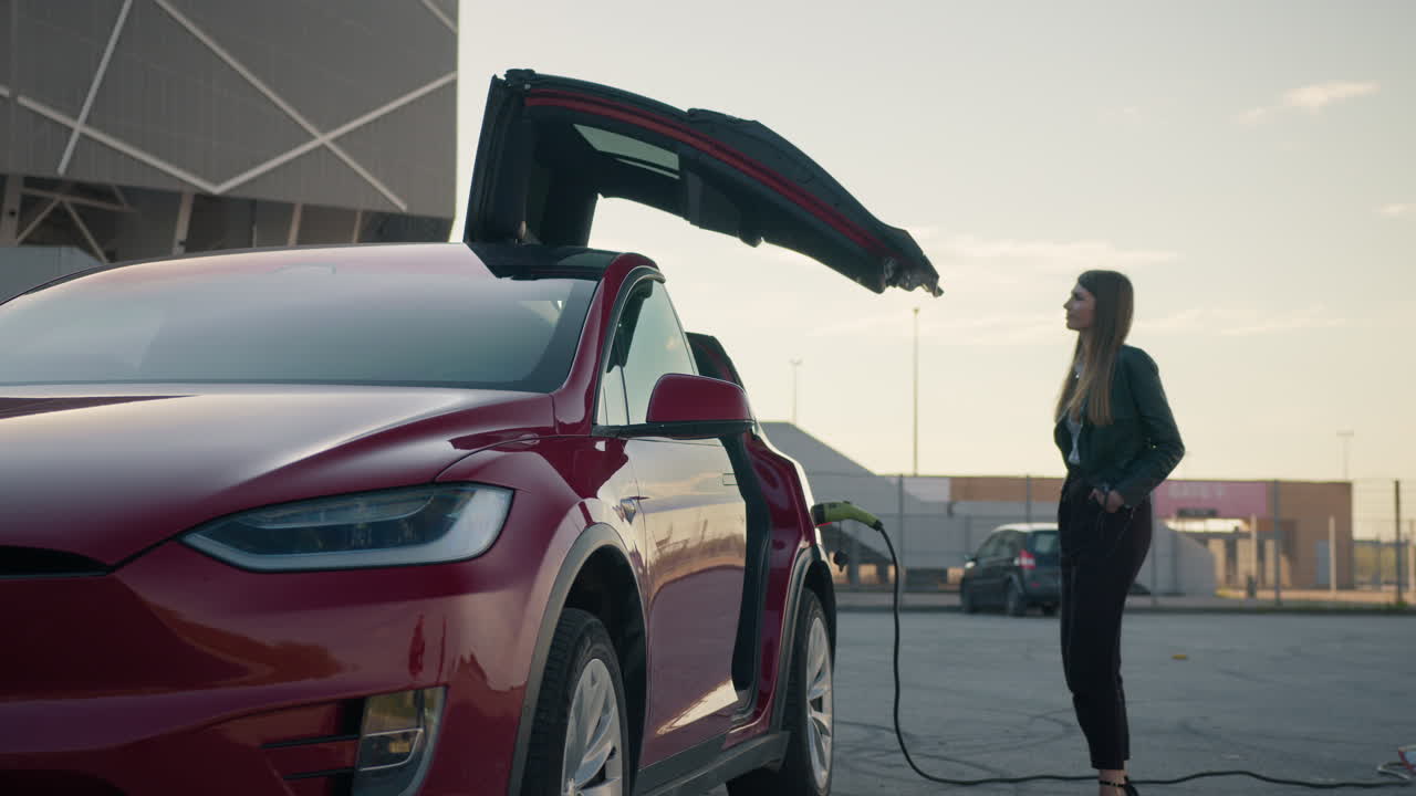 mujer cargando un suv eléctrico en una estación de carga fuera de un estadio