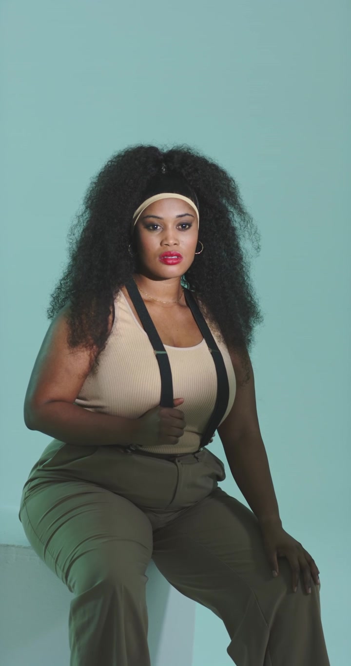 Vertical video: African American woman adjusting suspenders holding pose in studio for photoshoot