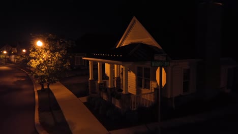 traditional american front house porch at night. aerial close up. night scene with lighting lantern lights in neighborhood. blooming trees outdoors on street.