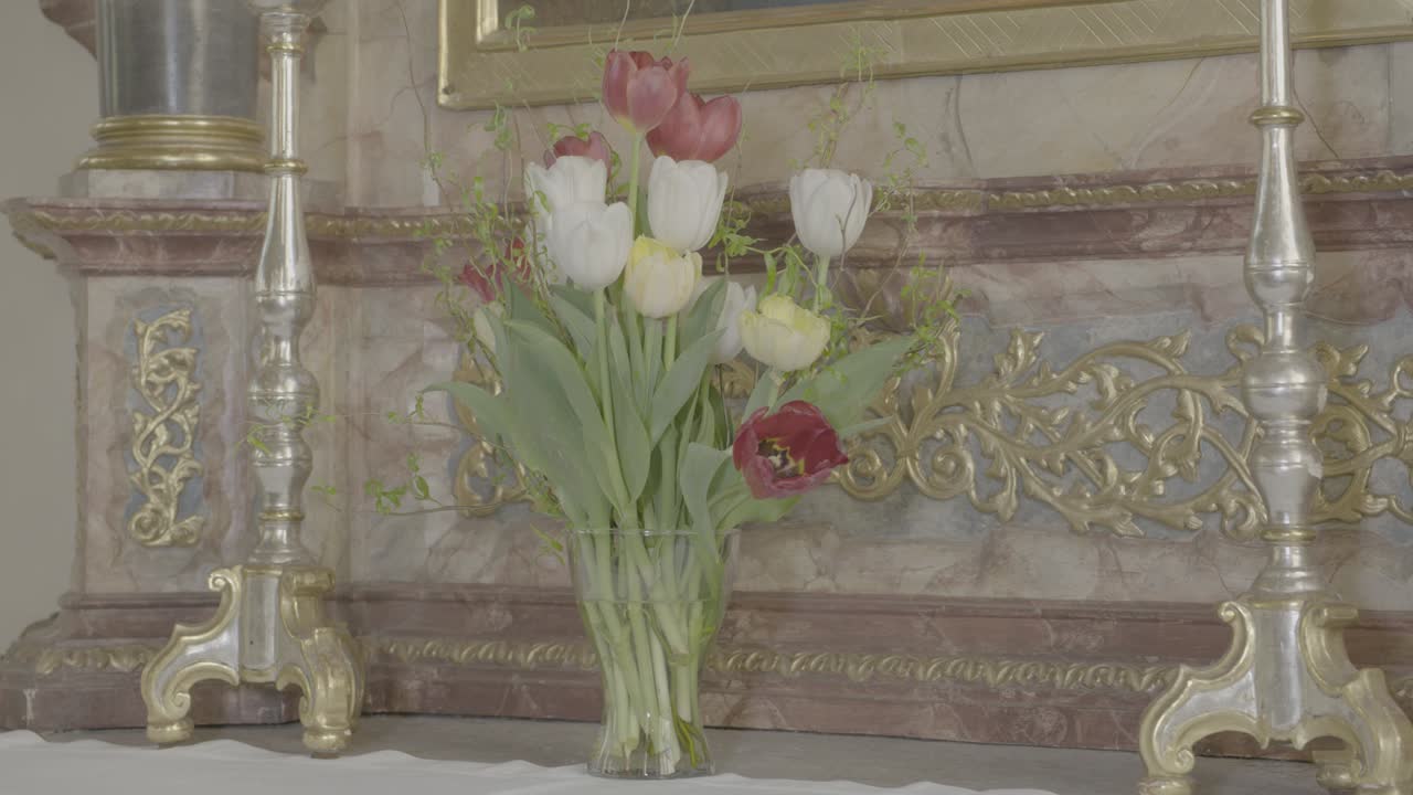 a vase with flowering tulips stands between two candlesticks on a baroque altar