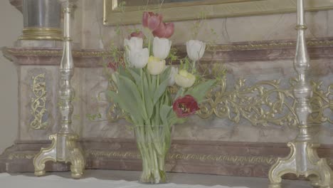 a vase with flowering tulips stands between two candlesticks on a baroque altar