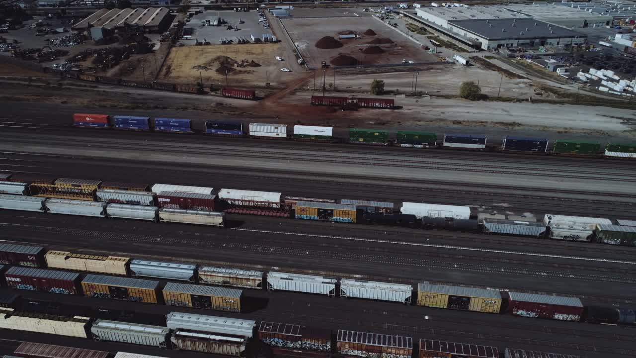 A panning drone shot of a busy rail yard with many trains on multiple tracks. 4K, UHD.
