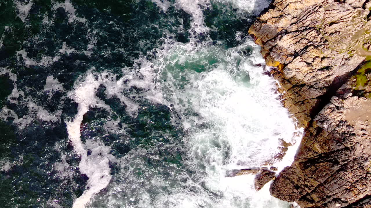 Onde oceaniche si infrangono su una costa rocciosa frastagliata e la schiuma si ritira, ripresa aerea.