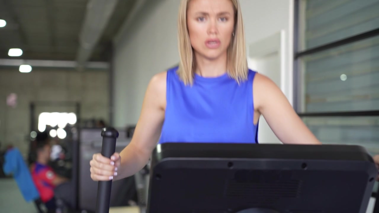 Una donna bionda si allena su un'ellittica in palestra durante la sua sessione di fitness.