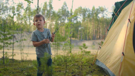 the boy helps his father to set up and assemble a tent in the forest. teaching children and travelling together in a tent camp