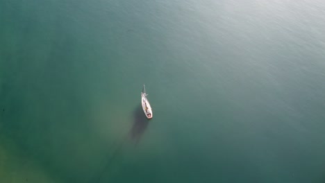 sail boat anchored in bay with pier in background