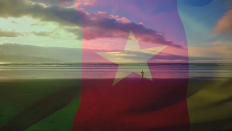 Digitale-Komposition-Einer-Schwenkenden-Kamerun-Flagge-Gegen-Einen-Mann,-Der-Am-Strand-Spaziert