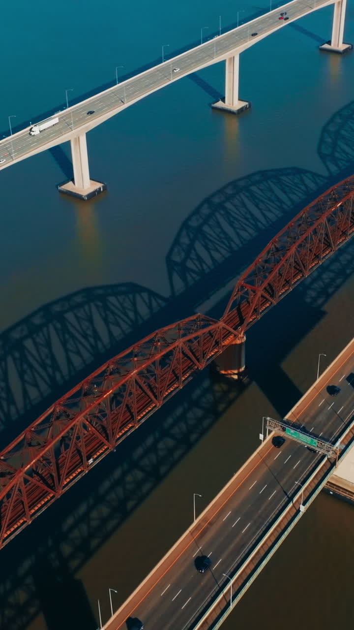 Beautiful simple bridges with one-way highways. Multiple cars moving by the bridges. Metal arched railway bridge in the middle. Vertical video