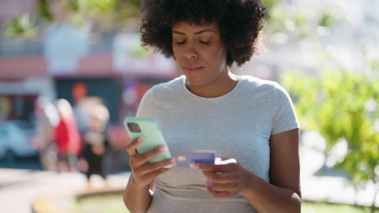 joven afroamericana usando teléfono inteligente y tarjeta de crédito en el parque