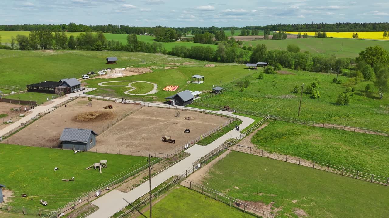 Tilting up drone shot of small countryside zoo with animal enclosures in rural landscape. Aerial footage of countryside zoo nestled in green farmland