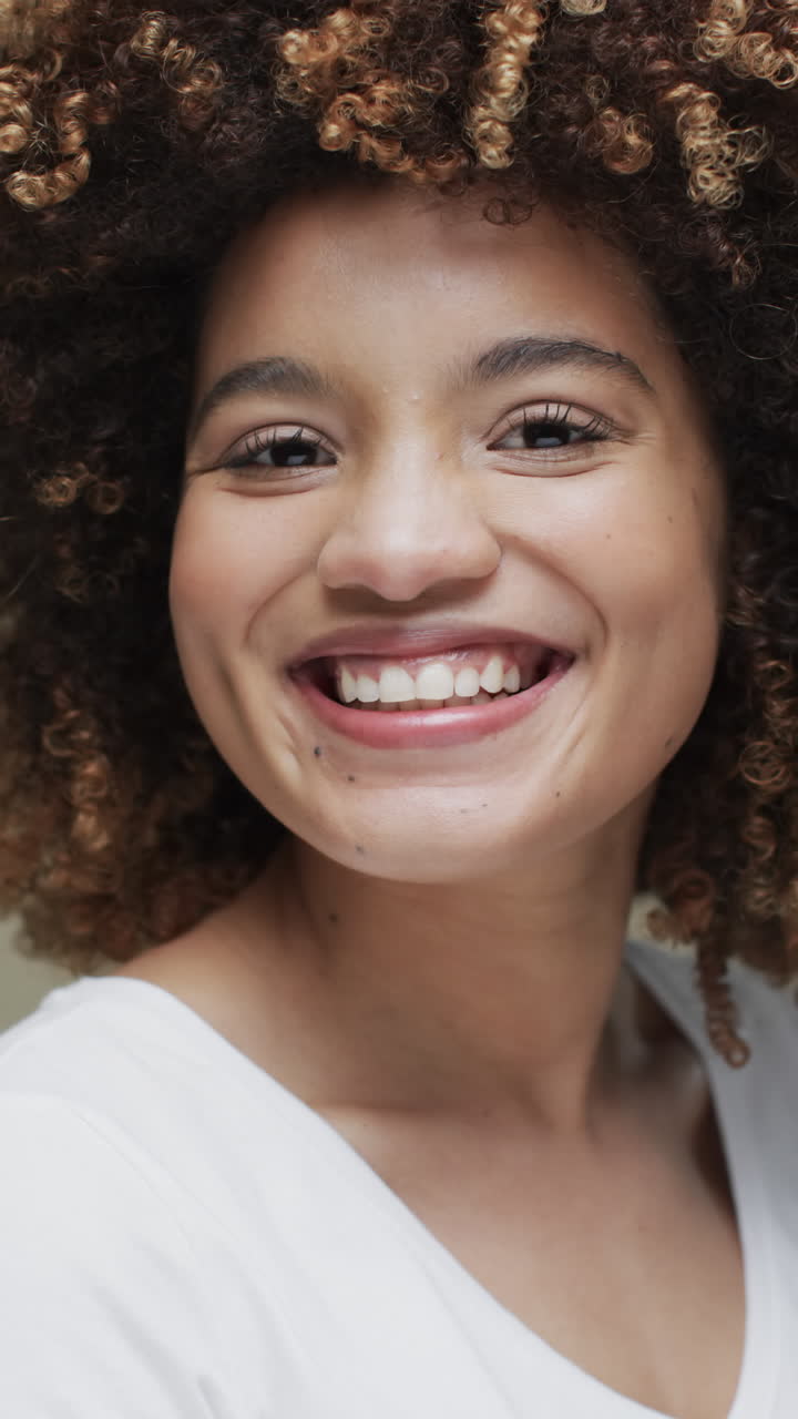 Vertical video of happy biracial woman with dark hair on beige background, slow motion