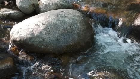 Una-Toma-Muy-Cercana-De-La-Superficie-De-Un-Río-Llena-De-Rocas-Siguiendo-La-Corriente