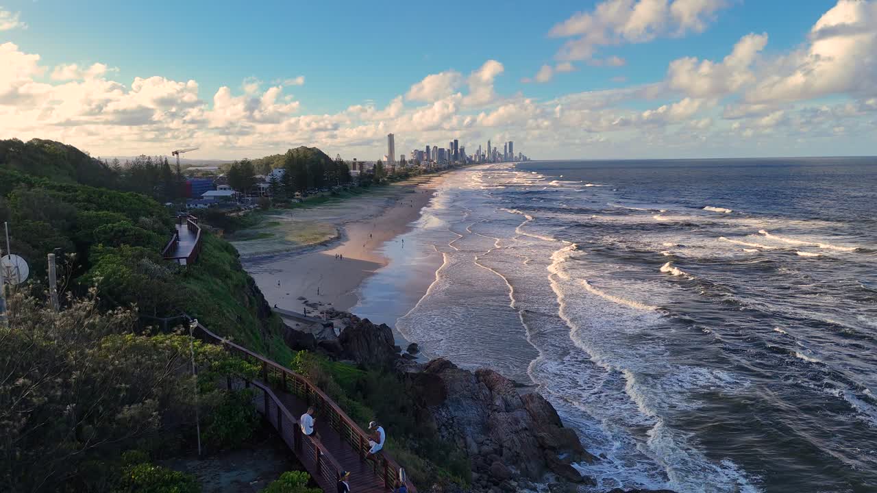 Aerial footage of Burleigh Heads beach with waves and coastal landscape under a clear sky