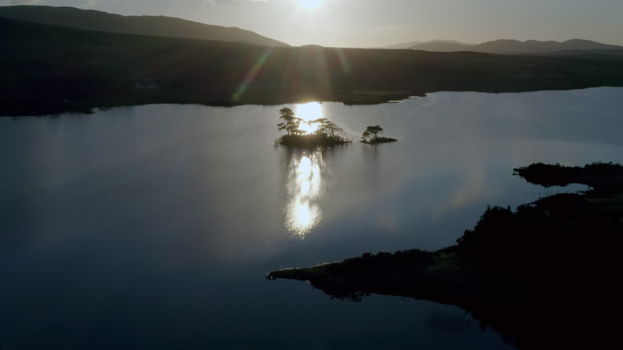 Lough Bofin backlit island glisten with strong sunlight, light reflecting off the mirror like surface of the lake, Connemara, Galway, Ireland