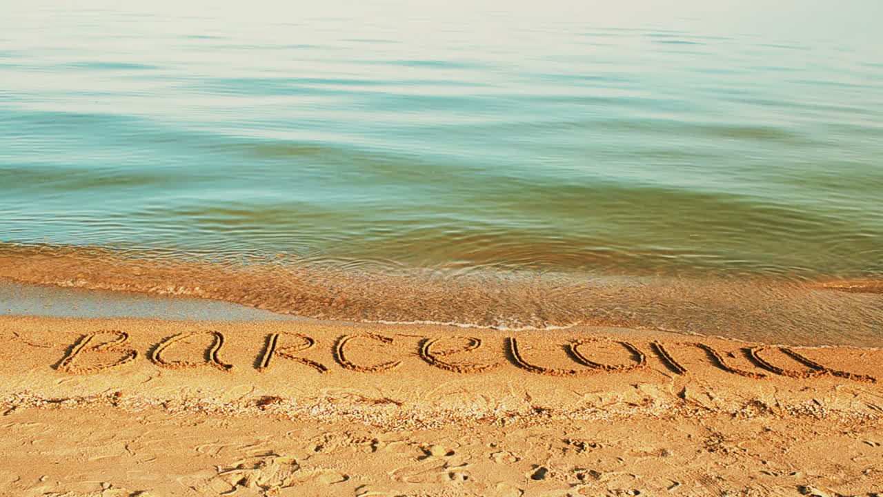 Indskriften 'Barcelona' i sandet på stranden.