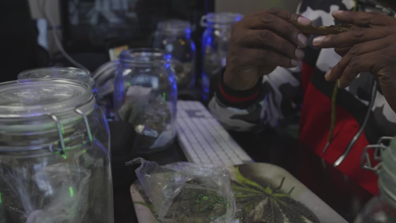 Filmato al rallentatore di un uomo di colore che riempie una cartina di tabacco con marijuana e la arrotola per formare un blunt.