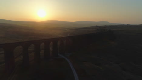 Luftdrohne-In-Die-Sonne-Geschossen,-Die-Sich-Von-Der-Ribblehead-Viadukt-Zugbrücke-Bei-Atemberaubendem-Sonnenaufgang-Im-Sommer-In-Yorkshire-Dales-England-Großbritannien-Mit-Hügeln-Im-Hintergrund-Zurückzieht