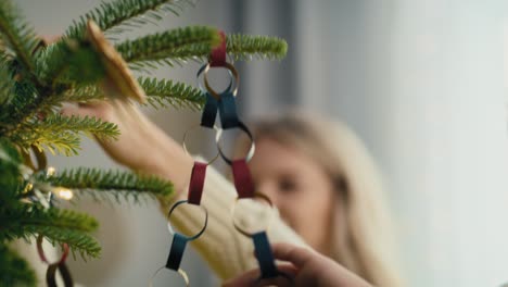 close up of caucasian little girl and mother decorating christmas tree with diy paper chain.