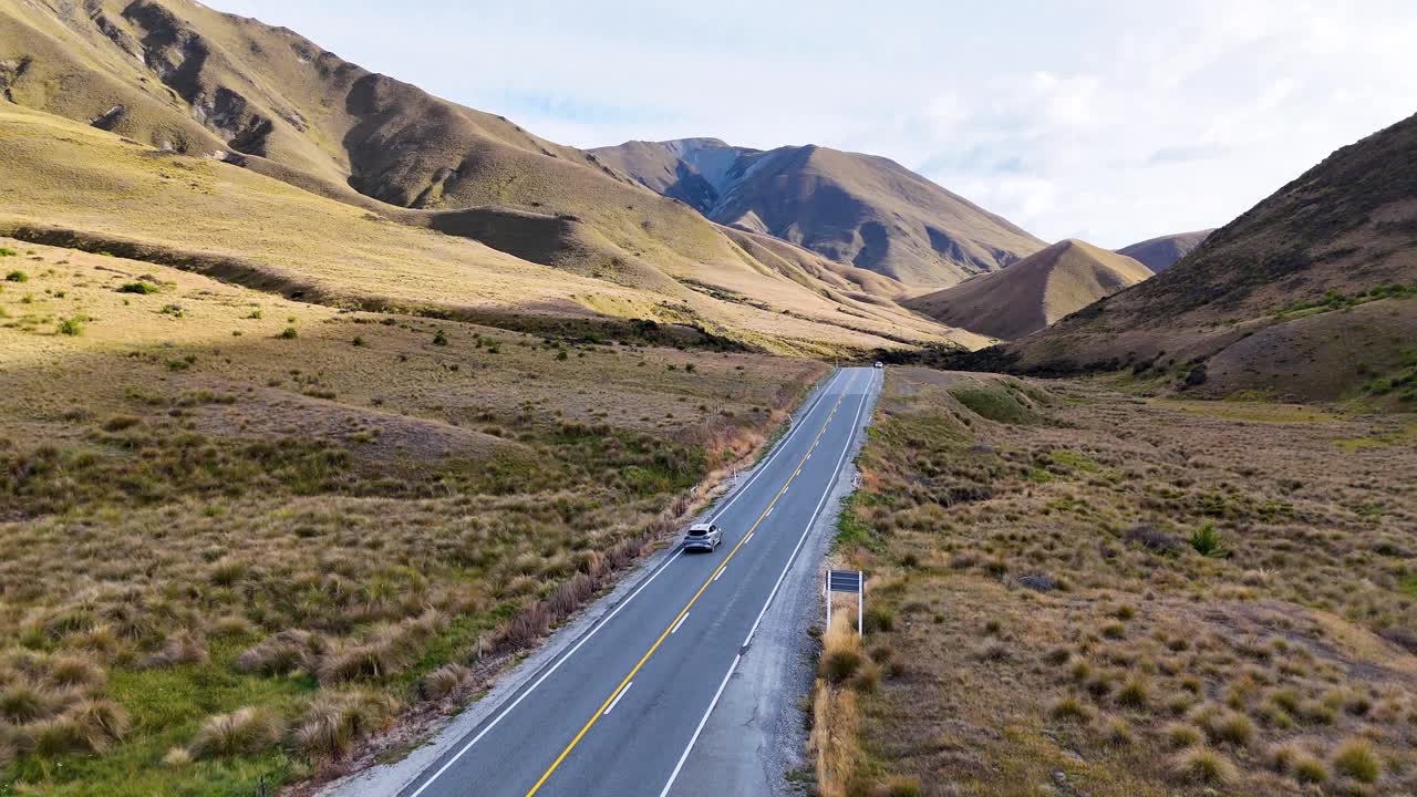 4K drone captures cars driving through Lindis Pass in New Zealand’s South Island. Winding roads, rolling hills, and mountains create a stunning alpine driving experience