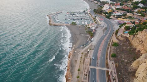 aerial birds eye shot of cars on road beside ocean with marina of malaga in background - static top down