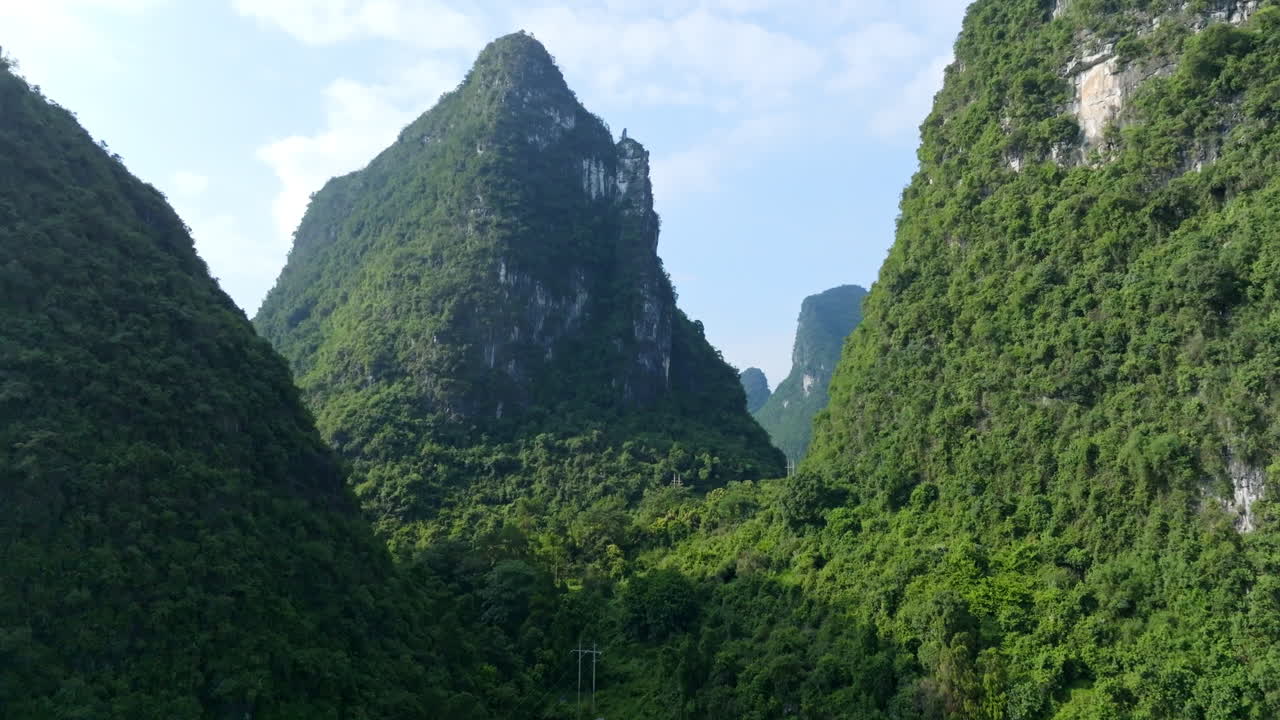 Drone ascending in front of towering, lush green mountains, in Xingping, China