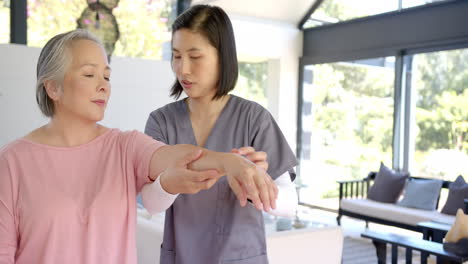 helping senior asian woman with arm exercises, physiotherapist providing home care therapy