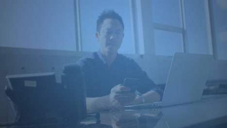 animation of multiple digital icons spinning over asian man using smartphone at office