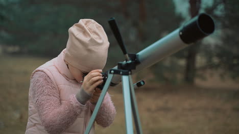 una ragazzina che guarda attraverso un telescopio nella foresta. bambini e scienza.