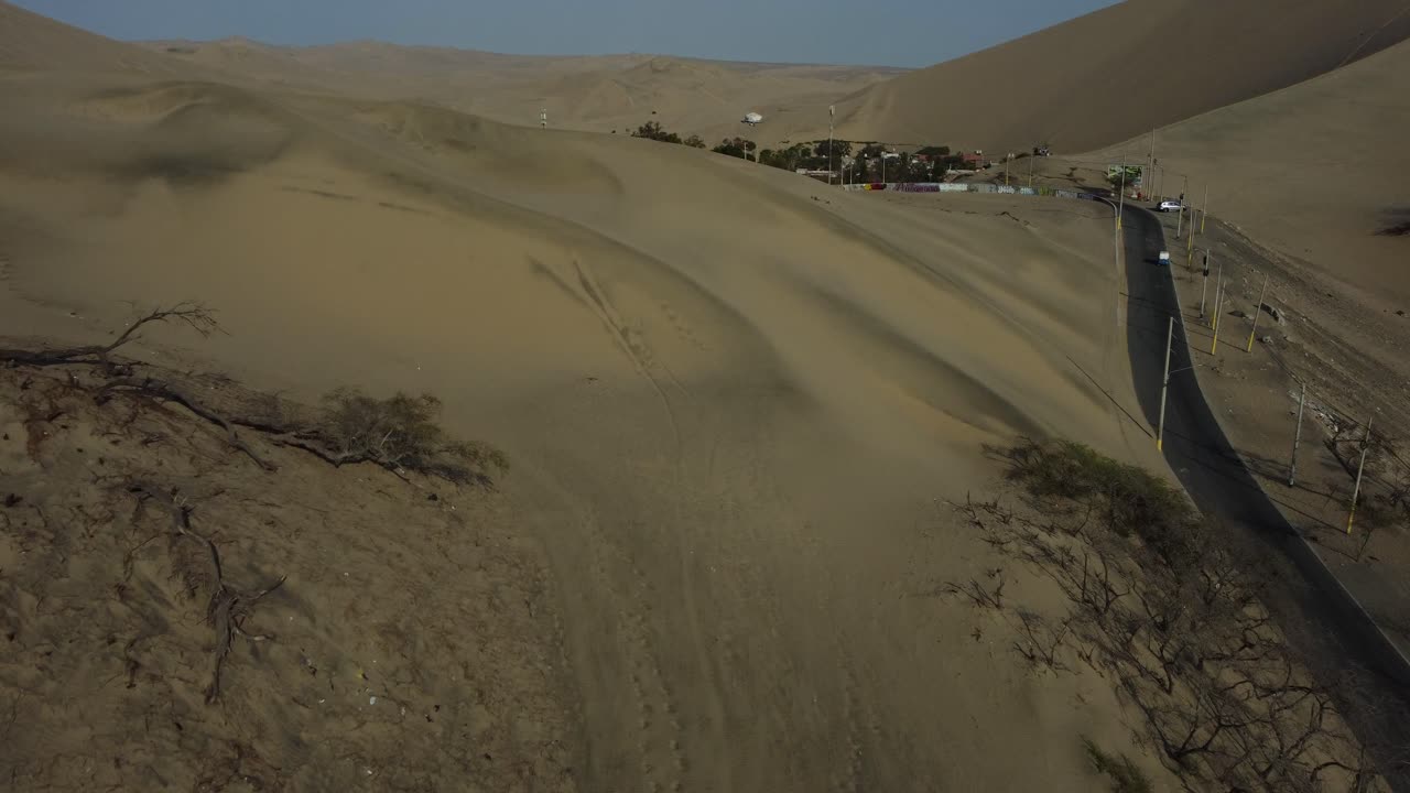 Aerial shot of an oasis in the desert surrounded sand dunes. Drone flies forward rising above a small hill revealing the hidden lagoon. Located in a place called "Huacachina" in Ica, Peru.