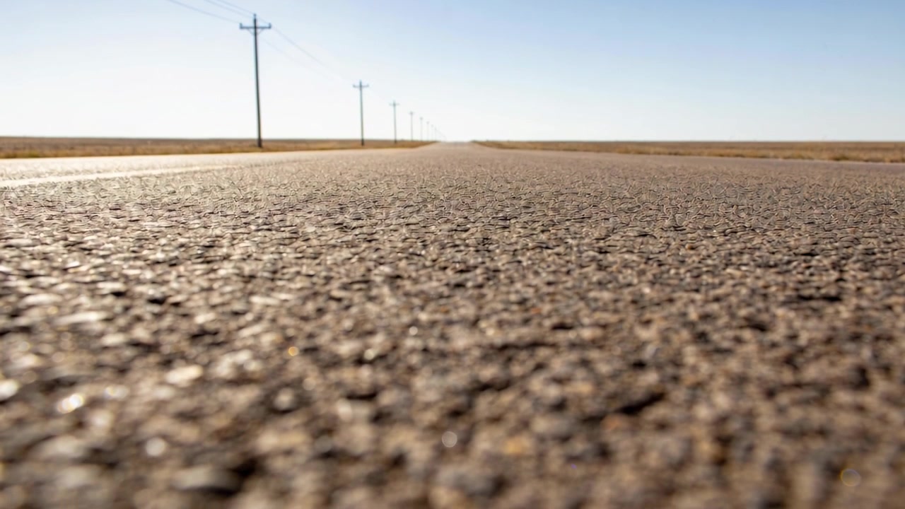 Câmera em ângulo baixo se movendo revelando a linha central de uma estrada áspera em direção ao horizonte em uma rodovia rural, com postes.