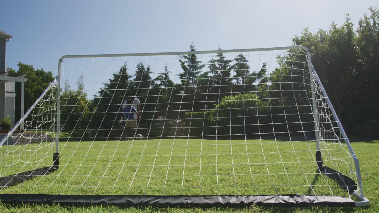 African male youth entering right dribbling kicking soccer ball at portable goal in yard practicing