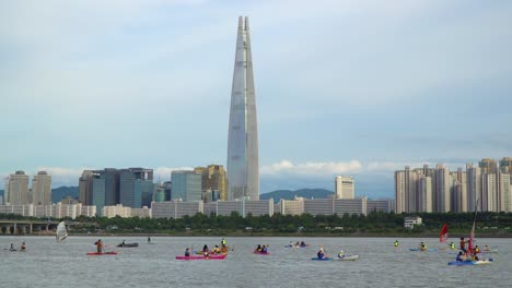 water sports activity - kayaking, windsurfing, paddleboarding - at han river with lotte world tower skyscraper in background in seoul, south korea