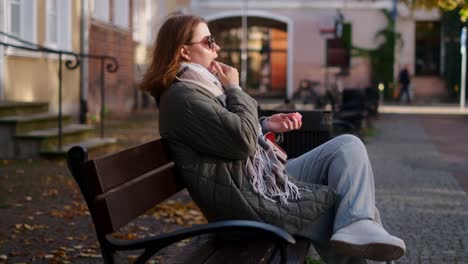 woman applying lipstick on a park bench